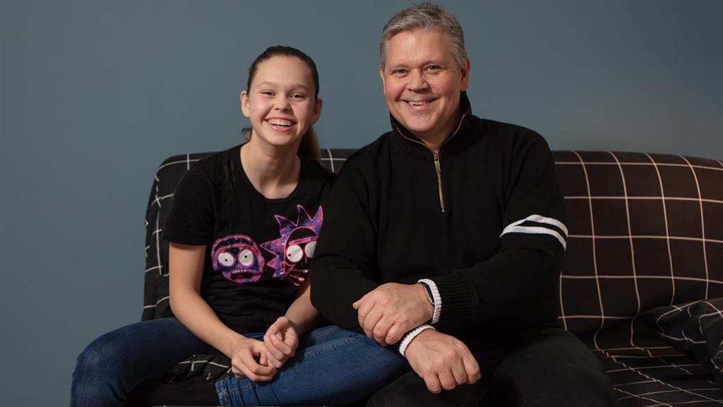 Far og datter som sitter i en sofa og smiler mot kamera. Fotografi.